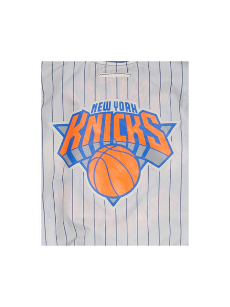 A vibrant plastic bag, reminiscent of the bold designs from Alpha Industries and New Era, showcases the New York Knicks logo alongside blue vertical stripes and a striking basketball graphic.