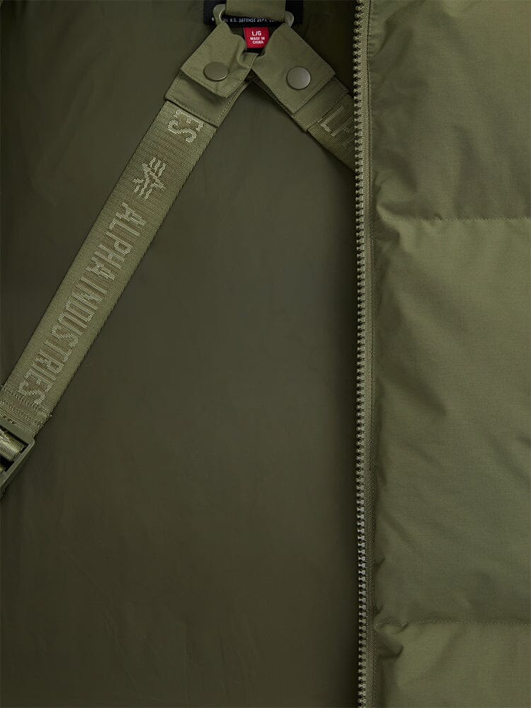 A close-up of the olive green Puffer Parka's interior showcases a zipper, snap buttons, and a strap printed with "Alpha Industries." 