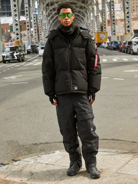 A person is standing under a steel bridge wearing the black Puffer Parka from Alpha Industries.