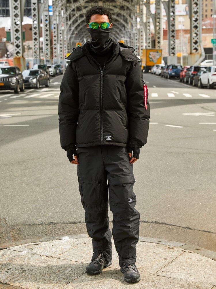 A person dressed in a black Puffer Parka from Alpha Industries, as they stand on a city street under a bridge.