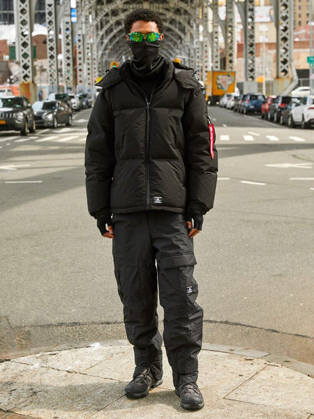 A person dressed in a black Puffer Parka from Alpha Industries, as they stand on a city street under a bridge.