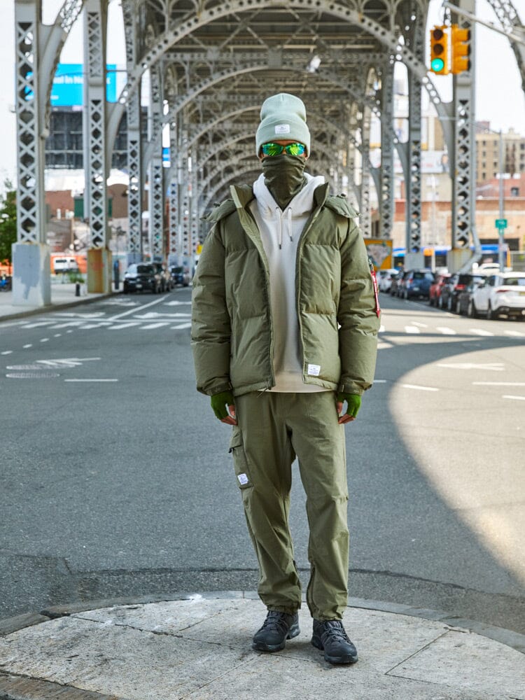 A person dressed in a green Puffer Parka from Alpha Industries, as they stand on a city street under a bridge.