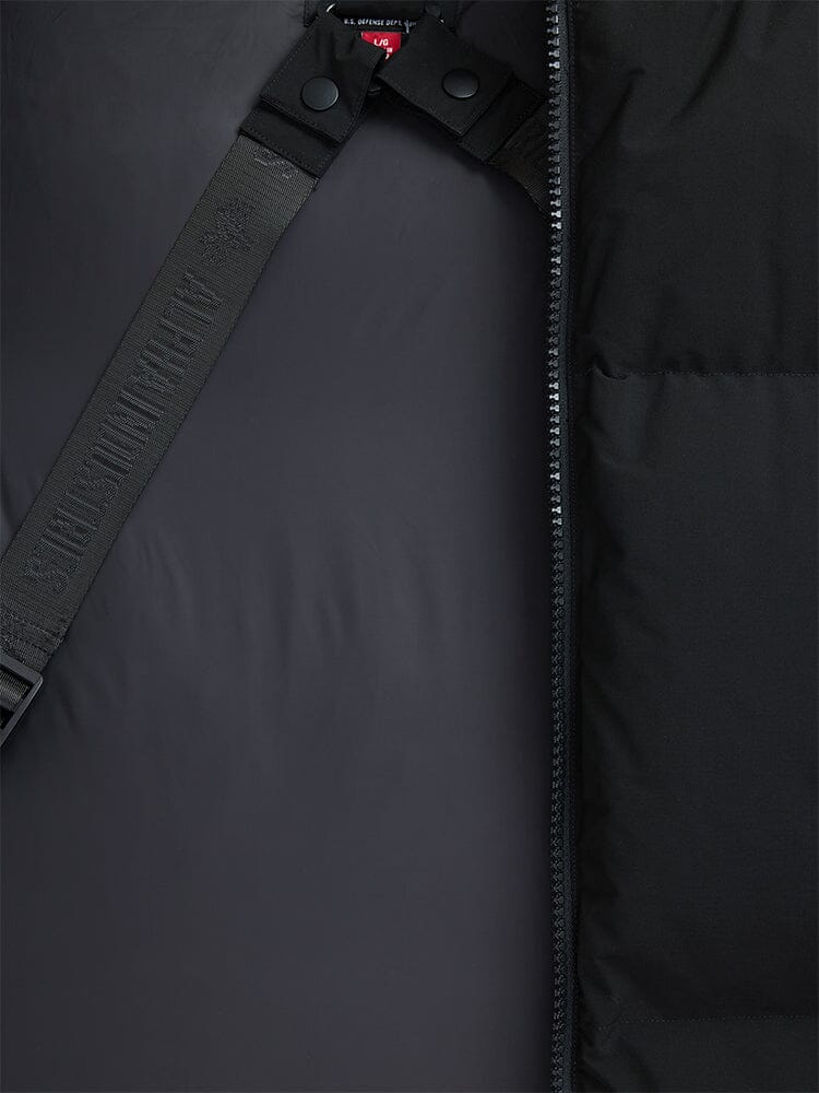 Close-up of the Alpha Industries Puffer Parka, showcasing a black padded design with a zipper and partially visible strap featuring embossed text.