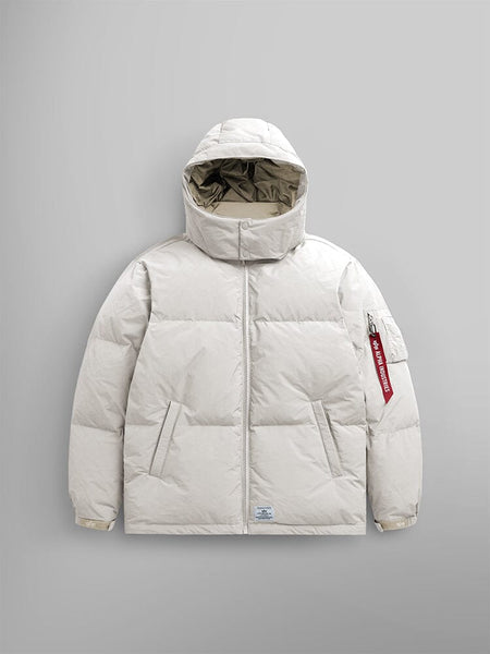 The limestone Puffer Parka by Alpha Industries is showcased with a removable hood and adjustable drawcords, along with a distinctive red tag on the sleeve.