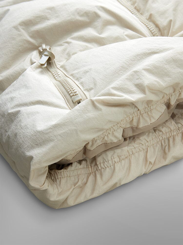 Sierra Short Puffer W by Alpha Industries, a beige puffer jacket with down fill and zipper, featuring an elastic hem, folded neatly.