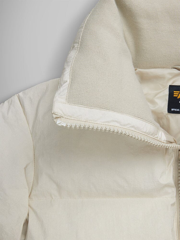 Close-up of the Sierra Short Puffer W in cream with a half-zipped collar, revealing the Alpha Industries label on the inside.